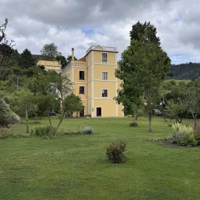 Yellow manor house surrounded by green lawns and trees in rural Galicia