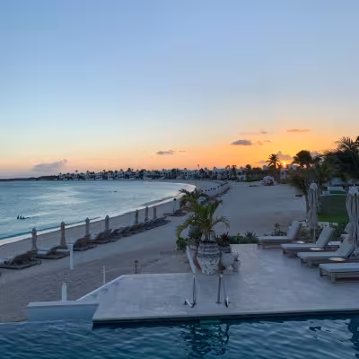 pool overlooking ocean with sunset in background and beach set up in anguilla