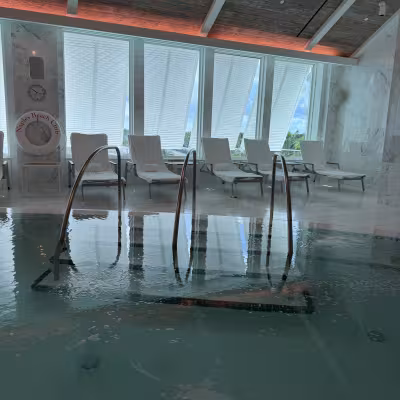 Serene indoor spa pool with bubbling water, metal handrails, and a row of white lounge chairs in front of tall windows letting in soft natural light