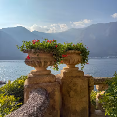Stone urns filled with red flowers overlooking Lake Como and the Italian Alps