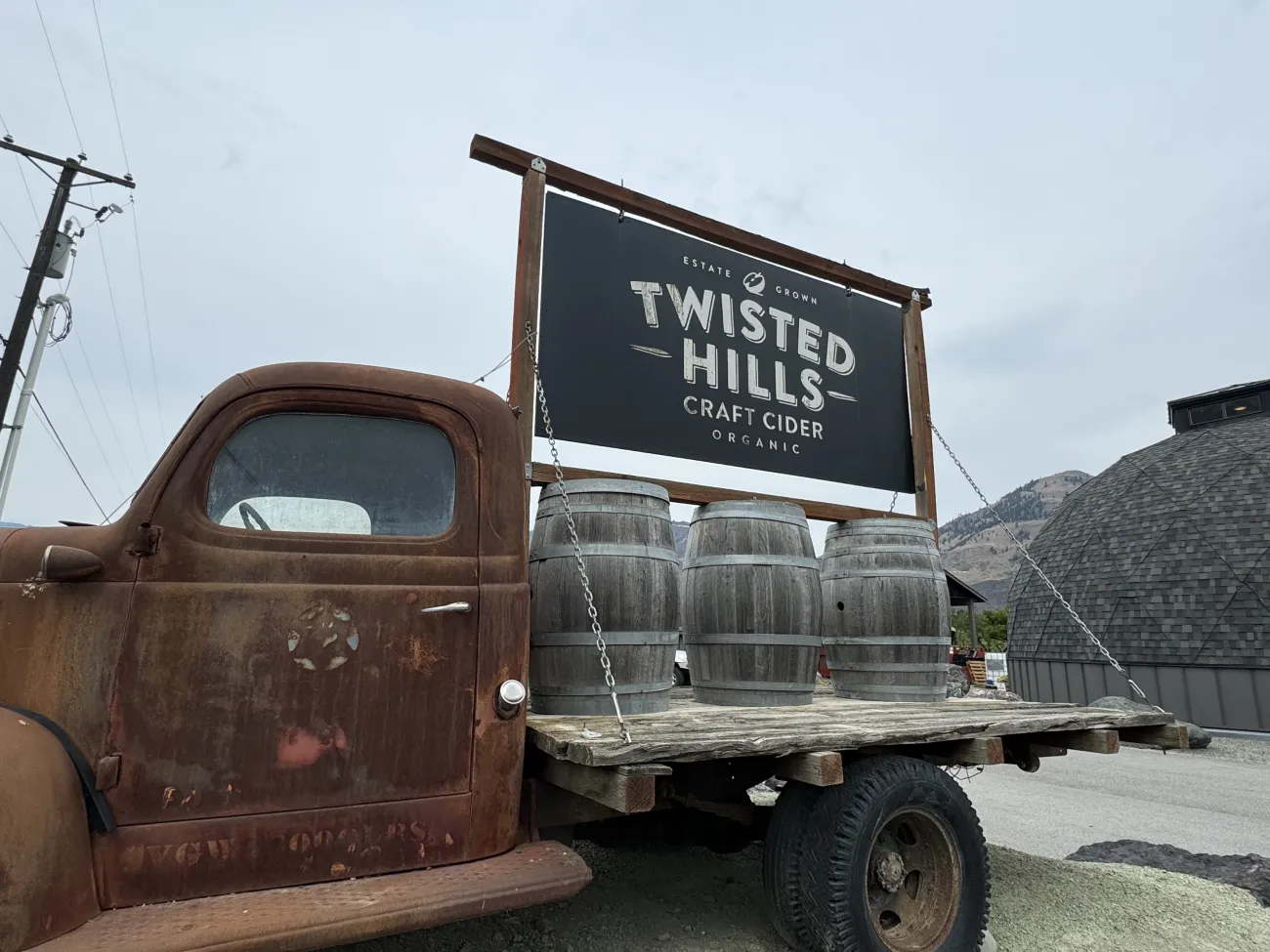 Rustic vintage truck displaying a Twisted Hills Craft Cider sign and wooden barrels