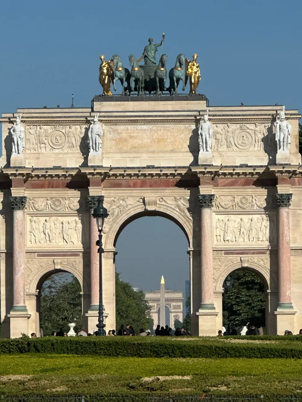 Triumphal arch in Paris with chariot statues and distant city landmarks framed beneath