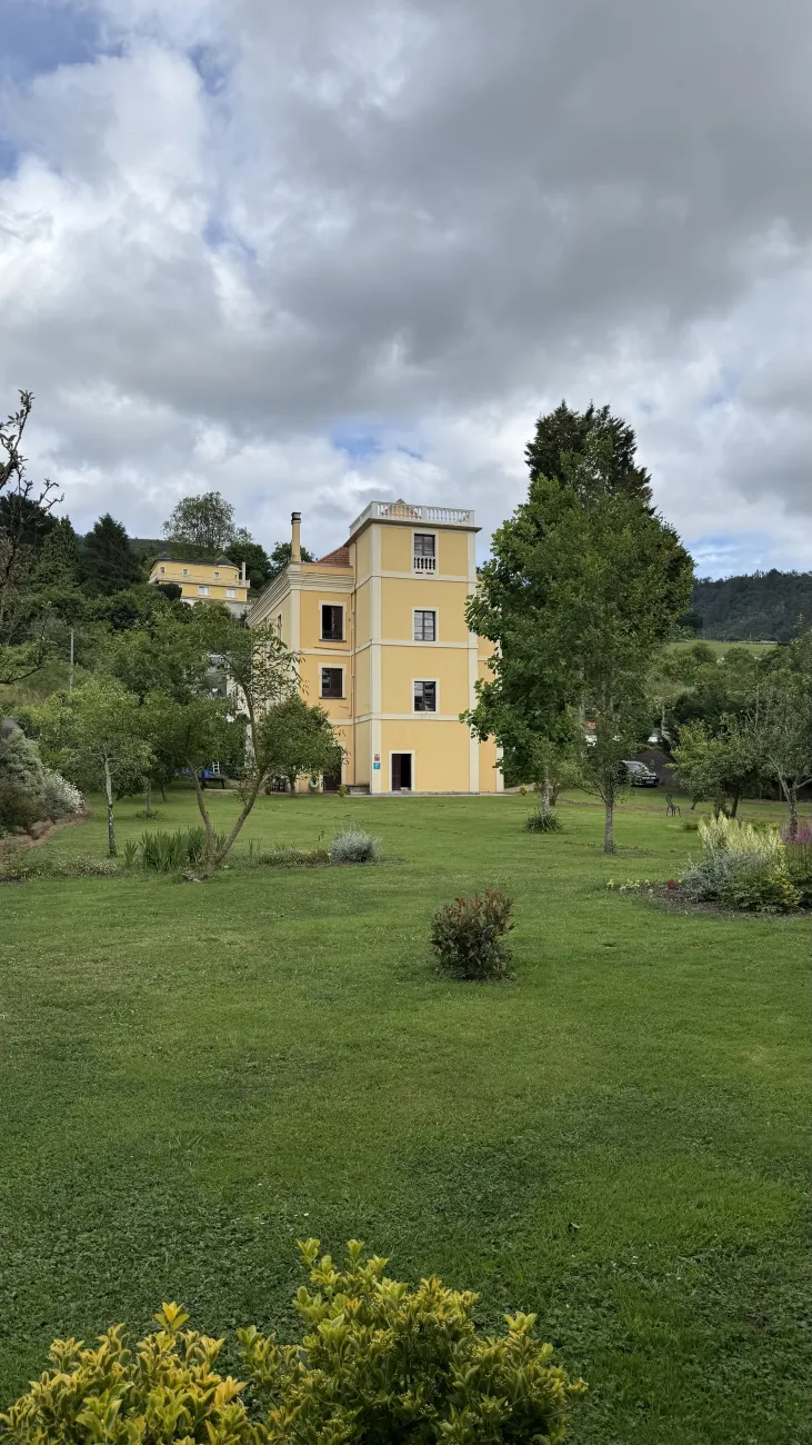 Yellow manor house surrounded by green lawns and trees in rural Galicia